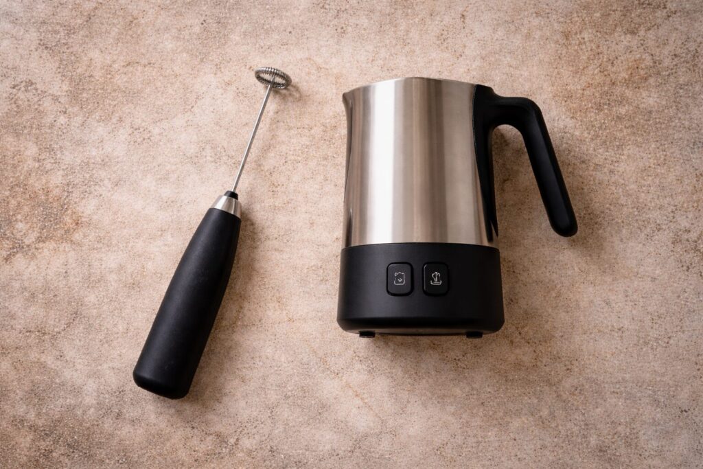 Handheld frother wand and electric milk frother on a linen surface
