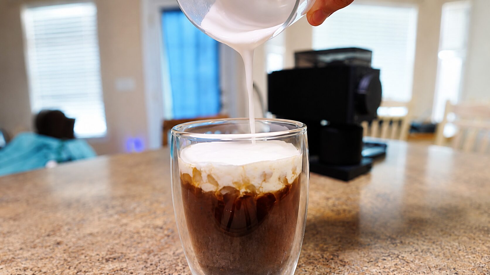 Pouring pistachio cold foam over a glass of cold brew