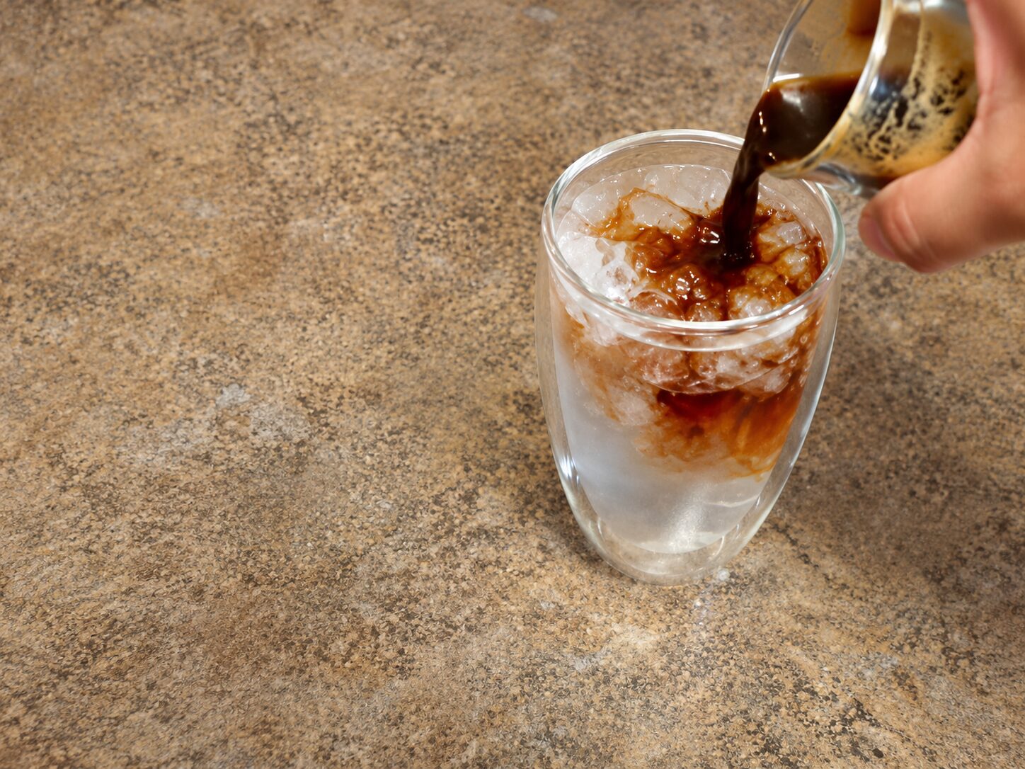 pouring skimmed espresso over iced water to finish an iced Americano